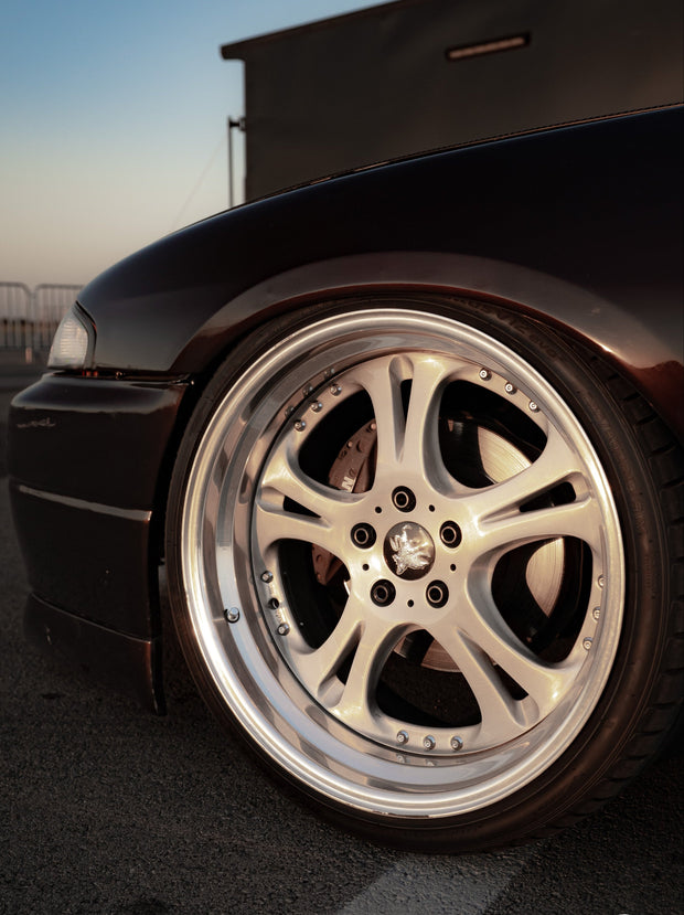 Close-up of a car wheel with a detailed rim on a road at sunset.